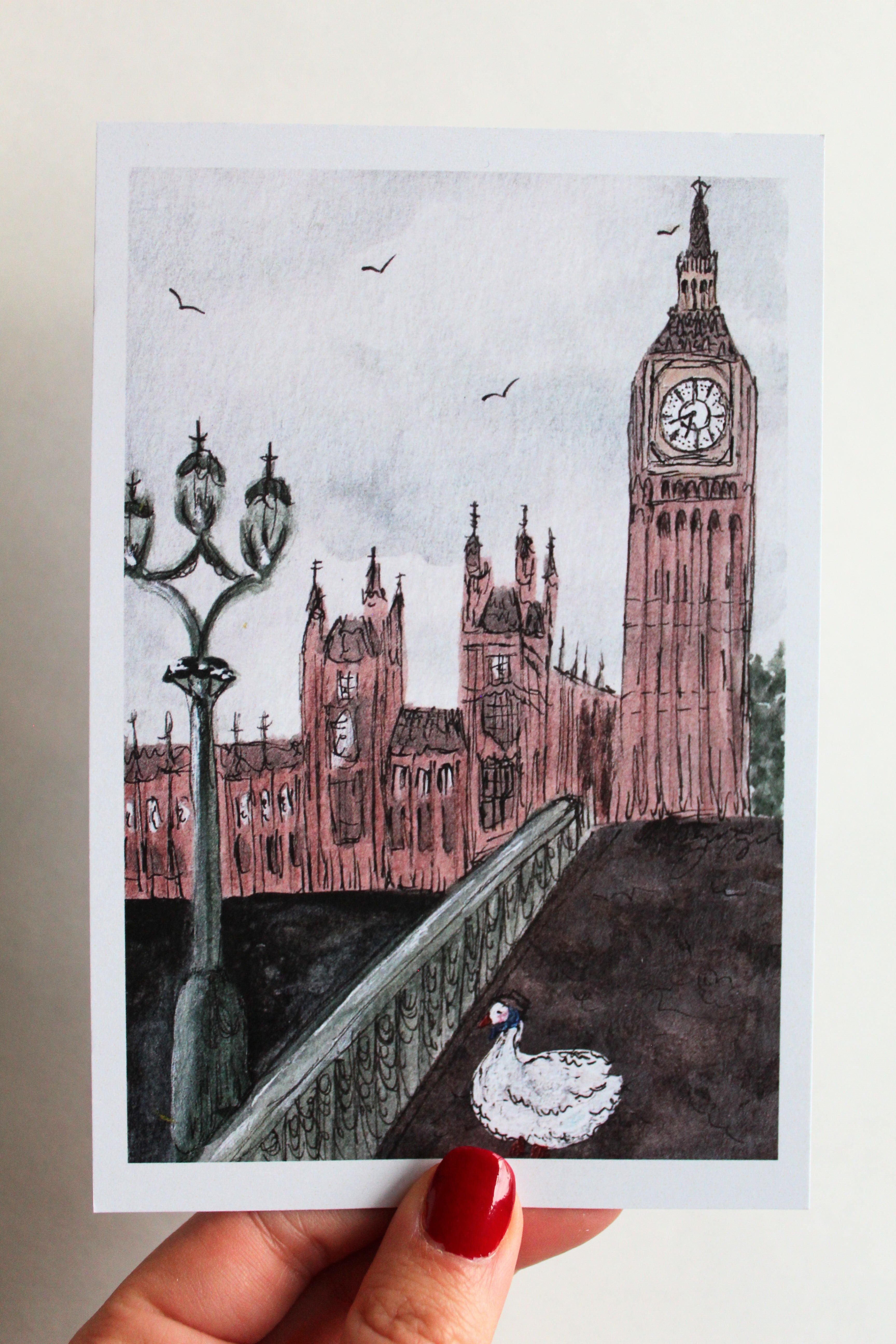 Postcard with an illustration of a duck in London, wearing a blue scarf and brown hat, walking on a bridge in front of Big Ben and Parliament. 
