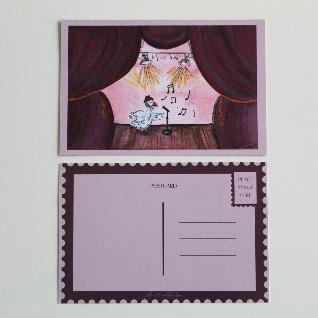 Postcard with an illustration of a duck performing on stage while wearing a brown hat and green scarf. The stage is made of brown wood and giant burgundy curtains with gold chords. Pictured with the back of the postcard where a letter can be written and address lines. 