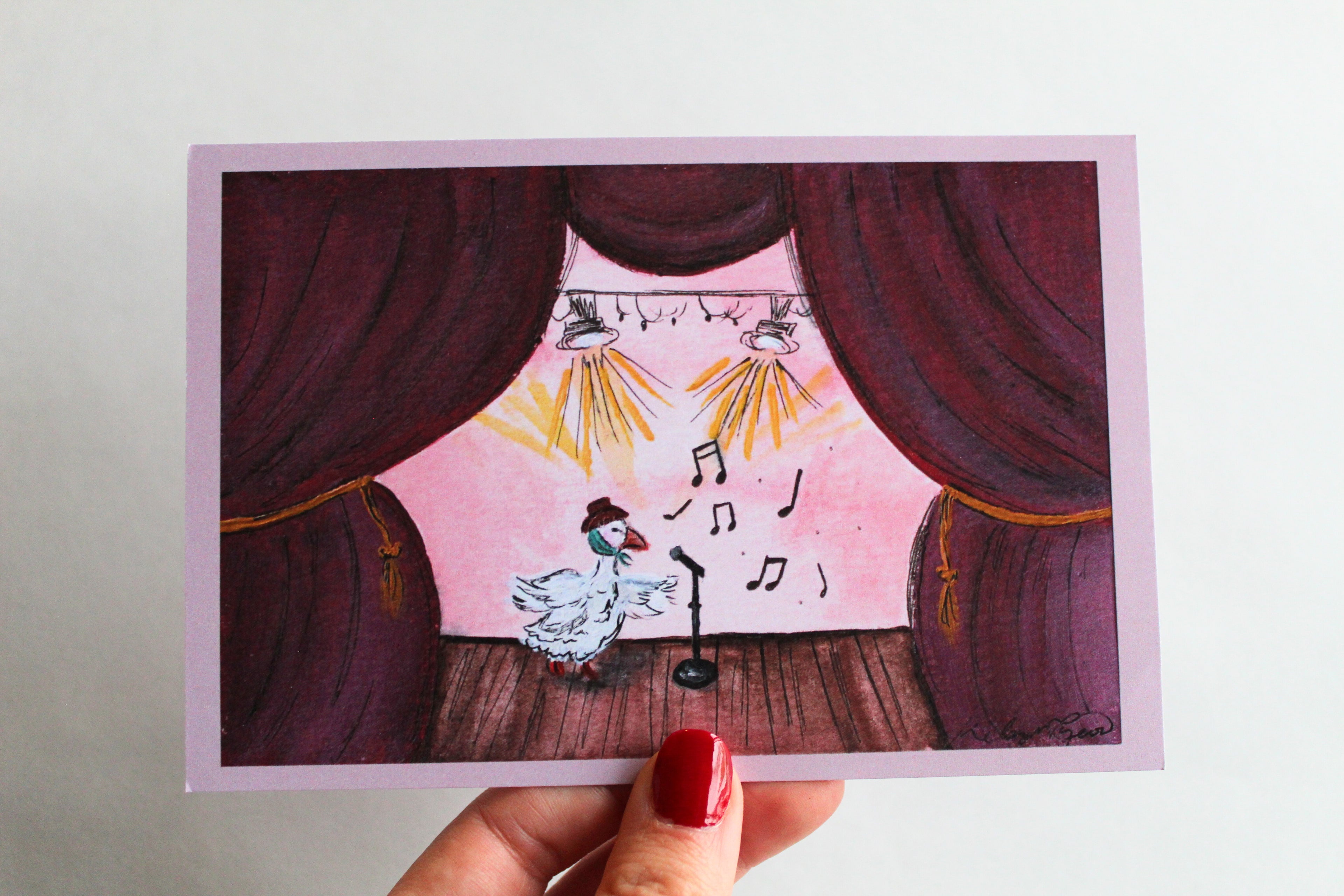 Postcard with an illustration of a duck performing on stage while wearing a brown hat and green scarf. The stage is made of brown wood and giant burgundy curtains with gold chords.