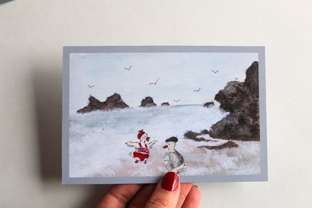 Postcard with an illustration of two ducks on a rocky and wavy beach, one wearing a red bathing suit and headband, and the other wearing a t-shirt and cap.