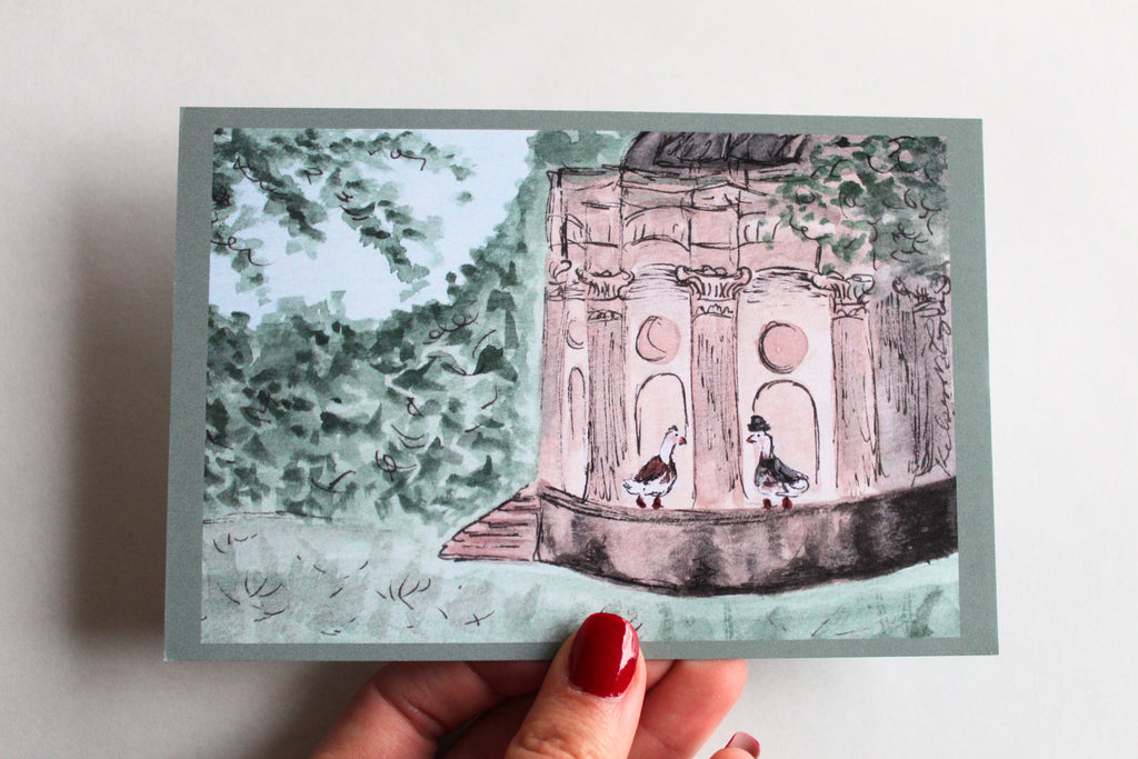 Postcard with an illustration of two ducks at the Temple of Apollo, one wearing a dress, and the other wearing a suit and hat, surrounded by leaves and trees.